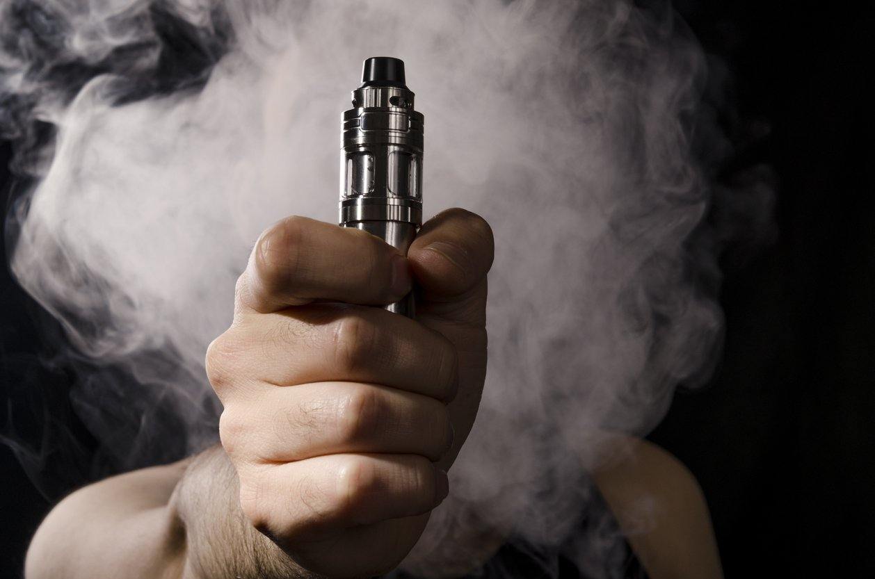 person holding vape pen with smoke in background