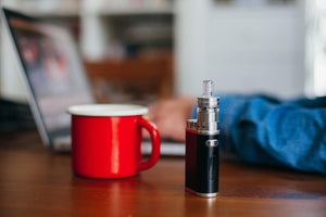 vaporizer and mug on desk person typing on laptop