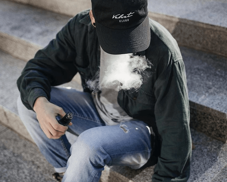 an aerial view of a man sitting on steps and vaping vegan, cruelty-free e-liquid