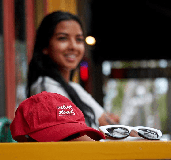a picture of a red Velvet Cloud hat in the foreground and a smiling girl in the background