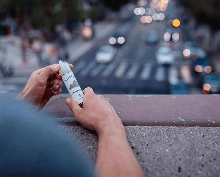 a man on a bridge holding a bottle of e-liquid overlooking a busy street