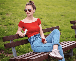 woman sitting on park bench in summer and vaping