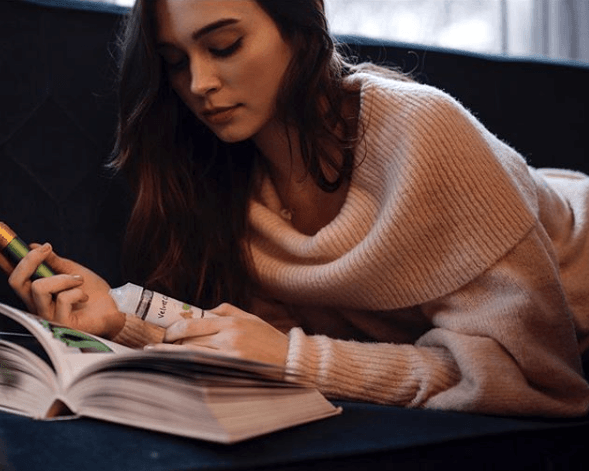 woman reading book on couch and vaping