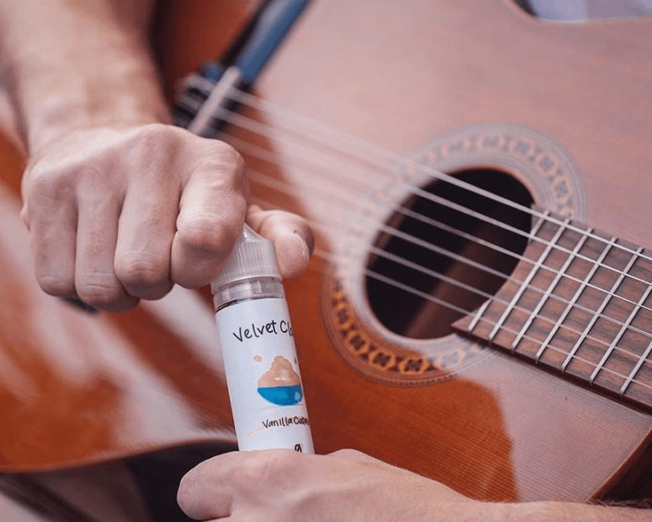 a man holding a guitar and a bottle of Velvet Cloud's vanilla custard e-liquid