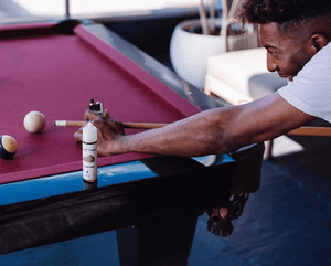 a man is playing pool with his Velvet Cloud e-liquid sitting on the pool table