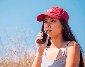 woman wearing a red Velvet Cloud hat vaping in a field