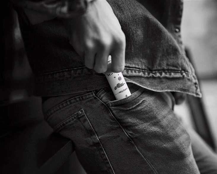 a black and white image of a man putting a bottle of Velvet Cloud e-liquid into his jeans pocket