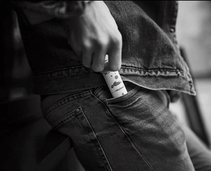a black and white image of a man putting a bottle of Velvet Cloud e-liquid into his jeans pocket