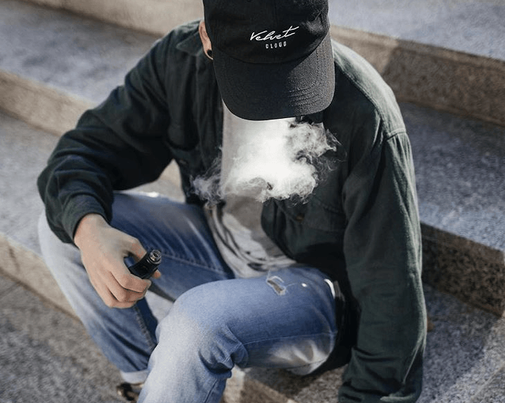 an aerial view of a man sitting on steps and vaping vegan, cruelty-free e-liquid