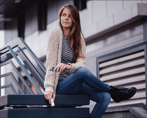 a woman sitting on a bench outdoors with a vape mod in one hand and velvet cloud e-liquid in the other