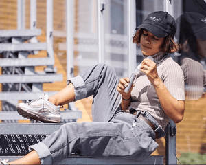 a woman in gray clothes and a Velvet Cloud hat vaping on a bench