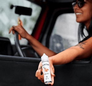 woman driving a car and holding peach-flavored e-liquid from Velvet Cloud