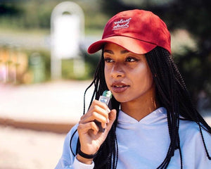 woman wearing a Velvet Cloud hat using a pod system to vape max VG e-liquids