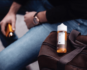 man holding vape pen with vape juice sitting on bag