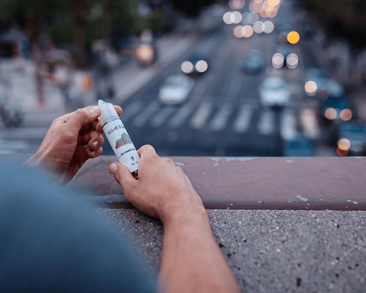a man on a bridge holding a bottle of e-liquid overlooking a busy street