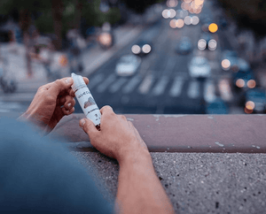 a man on a bridge holding a bottle of e-liquid overlooking a busy street